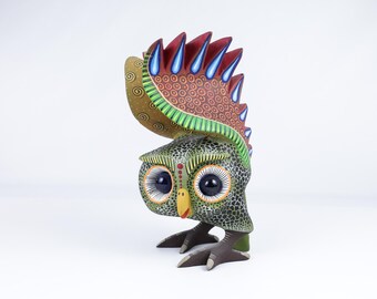 Könnte beinhalten: Handbemalte Eulenfigur. Die Eule hat einen gesprenkelten grünen Körper, große Augen und einen dekorativen Kamm mit roten, blauen und braunen Akzenten. Der Schnabel ist gelb und die Füße sind braun. Ein einzigartiges Dekorationsstück.