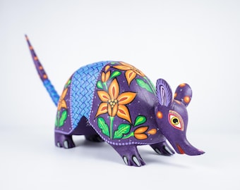 Könnte beinhalten: Handbemalte Holzfigur eines Gürteltiers. Der violette Körper ist mit orangefarbenen Blumendesigns, grünen Blättern und blauen geometrischen Mustern verziert. Der Schwanz ist blau und lila. Die Figur hat eine lange Schnauze und kleine Ohren.