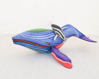 Könnte beinhalten: Eine handgeschnitzte Holzskulptur eines Wals mit aufwendigen Details und leuchtenden Farben, darunter Blau, Grün, Lila und Rot. Der Wal ist mit einem kleineren Fisch dargestellt, der neben ihm schwimmt.