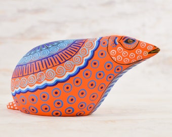Könnte beinhalten: Handbemalte orangefarbene Keramikfigur eines Gürteltiers mit blauen und weißen geometrischen Mustern. Das Gürteltier steht auf einer weißen Oberfläche.