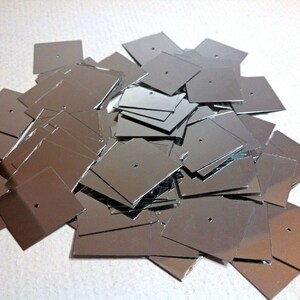 May include: A pile of silver square sequins with a small hole in the center of each sequin.