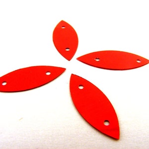 May include: Four red, oval-shaped, metal embellishments with two holes each. The embellishments are arranged in a star shape.