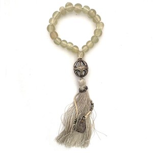 Może przedstawiać: Bransoletka z jasnozielonych szklanych koralików z srebrnym wisiorkiem i białym frędzlem. Wisiorek to kula o skomplikowanym wzorze, a frędzle mają mały srebrny wisiorek na końcu.
