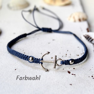 May include: A navy blue braided bracelet with a silver anchor charm and silver beads. The bracelet is adjustable and has a sliding knot closure.