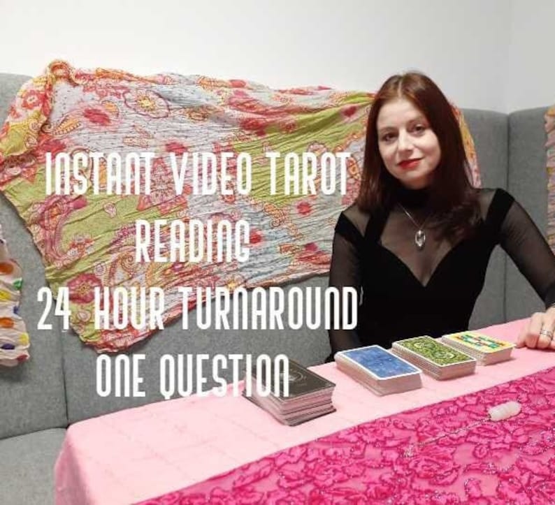 May include: A woman sits at a table with a pink tablecloth and a deck of tarot cards. The text on the table reads "Instant Video Tarot Reading 24 Hour Turnaround One Question."