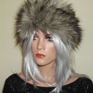 Puede incluir: Una diadema de pelo sintético gris con textura esponjosa. La diadema la lleva puesta un maniquí con el pelo plateado y un top negro brillante.