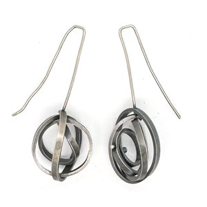 May include: A pair of silver dangle earrings with a geometric design. The earrings are made of multiple intertwined circles that form a sphere shape on one earring and an oval shape on the other.
