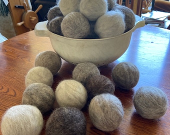 May include: A white colander filled with gray and brown wool dryer balls. The colander is sitting on a wooden table with more dryer balls scattered around it.
