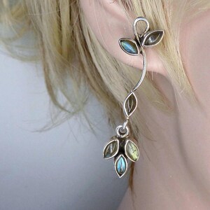 May include: A silver ear climber earring featuring a curved vine-like structure adorned with multiple marquise-cut labradorite gemstones. The stones exhibit iridescent blue and green flashes set within polished silver metal leaf-shaped settings.