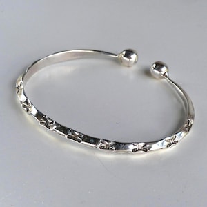 May include: A silver cuff bracelet with a textured band and two ball-shaped ends. The bracelet has a hammered design along the band. The open design allows for easy wear.