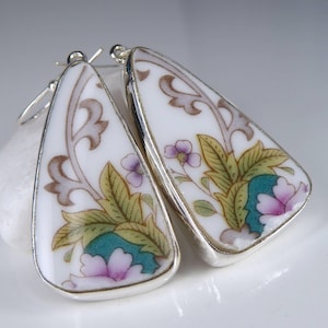 May include: A pair of silver earrings with a white porcelain design featuring floral patterns in shades of pink, purple, green, and gold.