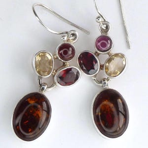 May include: A pair of sterling silver drop earrings featuring a cluster of multi-coloured gemstones. Each earring includes a large oval amber cabochon at the base, topped with smaller faceted oval and round stones in shades of garnet red, yellow, and purple.