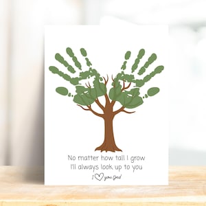Può includere: Una carta bianca con un disegno di albero fatto con impronte di mani verdi, con tronco e rami marroni. Il testo recita: "Non importa quanto crescerò, ti ammirerò sempre. Ti amo papà."