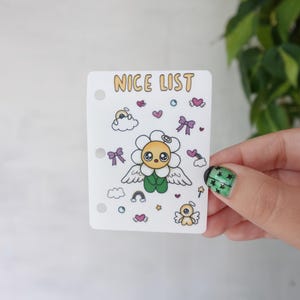 May include: A rectangular white sticker with three punched holes on the left side, featuring the text NICE LIST in yellow. The design includes a central yellow flower character with white wings, surrounded by small icons of hearts, bows, and clouds.