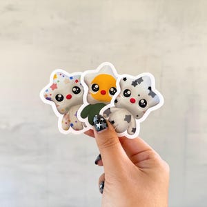 May include: Three die-cut stickers shaped like stars with cartoon faces. One sticker has a white base with colorful star patterns, one has a yellow center with a dark green base, and one has a white base with black cow-like spots.