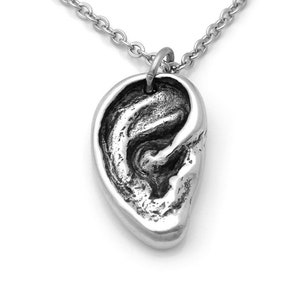 May include: A silver necklace with a detailed ear pendant. The pendant is a realistic depiction of an ear, with all the intricate details of the earlobe, helix, and concha.
