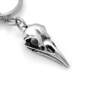 May include: Silver bird skull keychain with a silver key ring. The skull is detailed and has a realistic look.