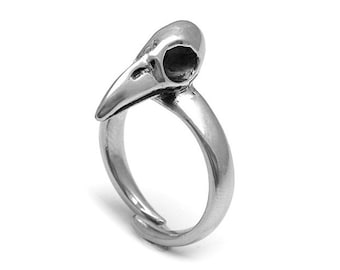 Puede incluir: Anillo plateado con diseño de calavera de pájaro. La calavera tiene un pico puntiagudo y una cuenca ocular hueca. La banda del anillo es lisa y ajustable, con un diseño simple y elegante.