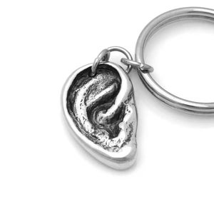 May include: A silver keychain with a detailed ear charm. The charm is attached to a silver key ring.