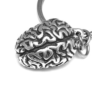 Può includere: Un portachiavi in ​​argento con un design anatomico dettagliato del cervello. Il portachiavi è attaccato a un anello in argento.