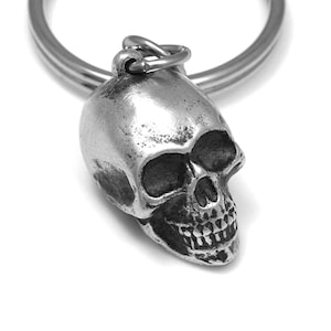 May include: A silver skull keychain with a detailed design. The skull has a textured surface and a realistic appearance.