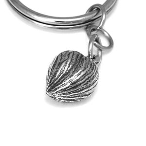 Puede incluir: Un llavero de plata con un dije en forma de corazón texturizado y detallado. El dije se parece a una nuez o una semilla.
