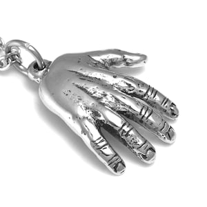 May include: A silver pendant necklace featuring a detailed hand design. The hand is open with all five fingers extended. The pendant is attached to a silver chain.