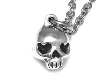 May include: A silver skull pendant necklace with heart-shaped eyes. The necklace has a silver chain.