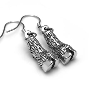 May include: A pair of silver-colored earrings shaped like animal hooves. The earrings have a textured surface and are suspended from simple ear wires. The hooves are detailed with a split at the bottom.