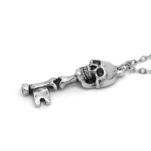 May include: A silver skull key pendant necklace. The key is detailed with a skull head and a traditional key shape. The necklace is made of a silver chain.