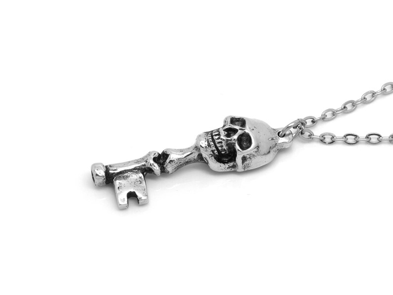 May include: A silver skull key pendant necklace. The key is detailed with a skull head and a traditional key shape. The necklace is made of a silver chain.