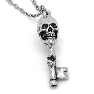 May include: A silver skull key pendant necklace. The skull is detailed with eye sockets, a nose, and a mouth. The key is a simple design with a small bow at the bottom.