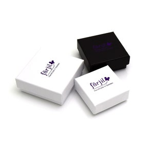 May include: Three small jewelry boxes, two white and one black, are arranged on a white surface. The boxes have a square shape with a lid. Each box features the word "f&auml;rjil" in a purple font, along with a purple flower graphic and the text "Handmade in Sweden."