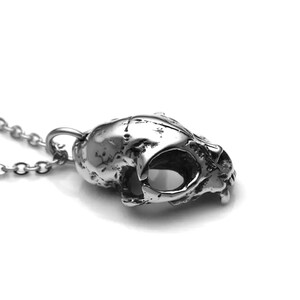 May include: A silver skull pendant necklace with a detailed, textured design. The skull is slightly tilted to the side, showing the eye sockets and teeth.
