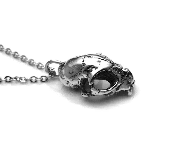 May include: A silver skull pendant necklace with a detailed, textured design. The skull is slightly tilted to the side, showing the eye sockets and teeth.
