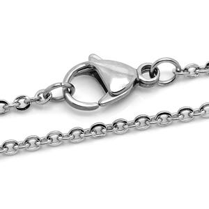 May include: A close-up of a silver-colored necklace chain with a lobster clasp. The chain is made of small, round links. The clasp is a shiny, polished metal. The necklace is displayed against a white background.