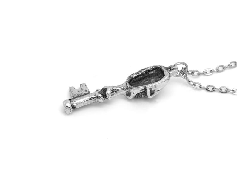 May include: A silver key pendant necklace with a skull-shaped keyhole. The chain is silver and has a delicate link design.