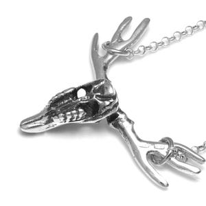 May include: A silver necklace with a detailed deer skull pendant. The pendant features a skull with antlers and a chain.