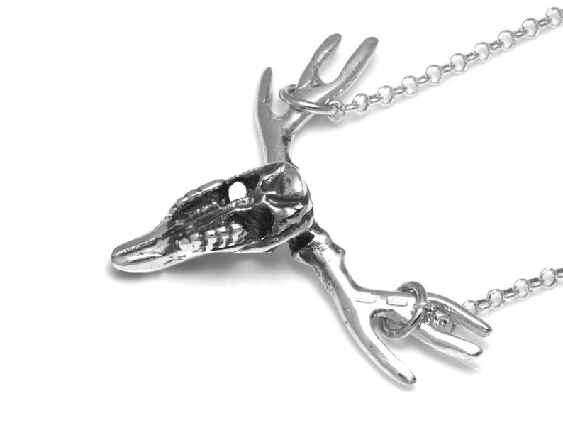 May include: A silver necklace with a detailed deer skull pendant. The pendant features a skull with antlers and a chain.