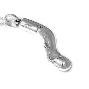 May include: A silver pendant necklace with a unique, abstract, organic-shaped charm. The charm is smooth and has a textured surface.