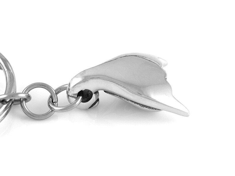 May include: A silver-toned keychain with a stylized heart-shaped charm. The charm is smooth and has a slightly curved shape.