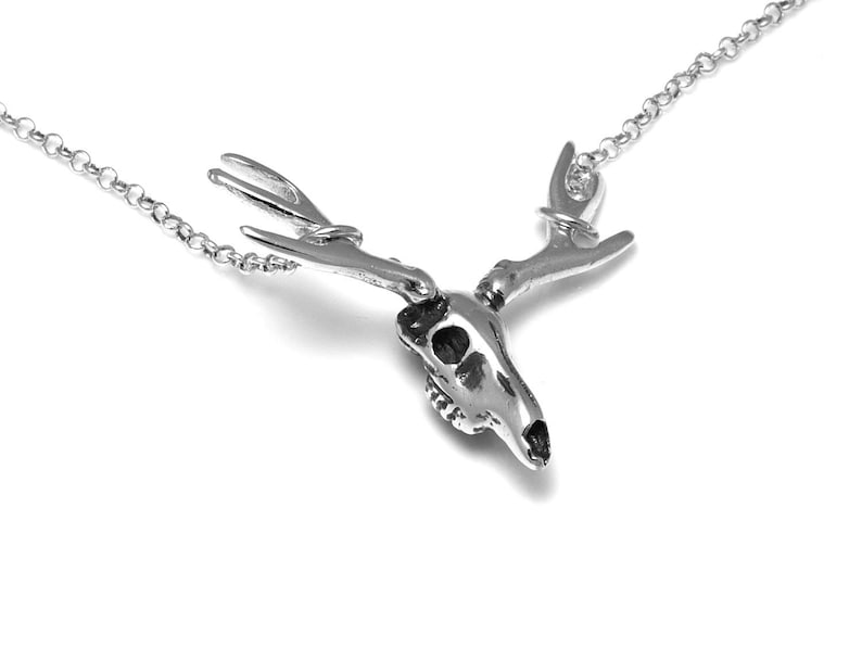 May include: A silver deer skull necklace with a detailed design of the skull and antlers. The necklace is on a silver chain.