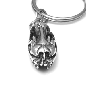 Pu&ograve; includere: Un portachiavi d'argento con un designo astratto tridimensionale dettagliato. Il design ricorda un teschio o una testa di animale stilizzata.