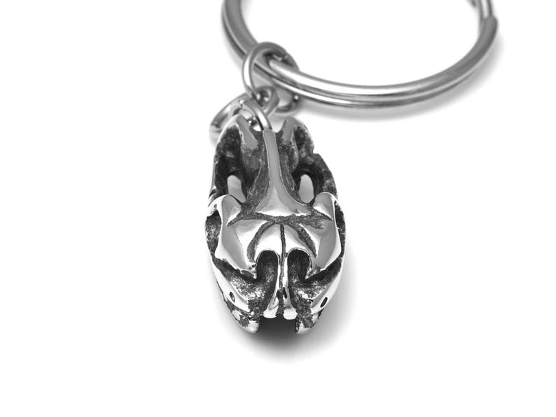 Pu&ograve; includere: Un portachiavi d'argento con un designo astratto tridimensionale dettagliato. Il design ricorda un teschio o una testa di animale stilizzata.