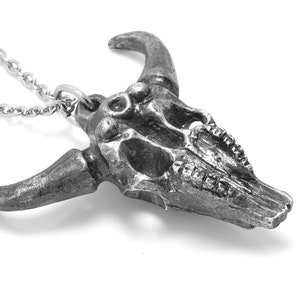 May include: A silver bull skull pendant necklace. The skull is detailed with teeth and horns. The chain is silver and has a lobster clasp.