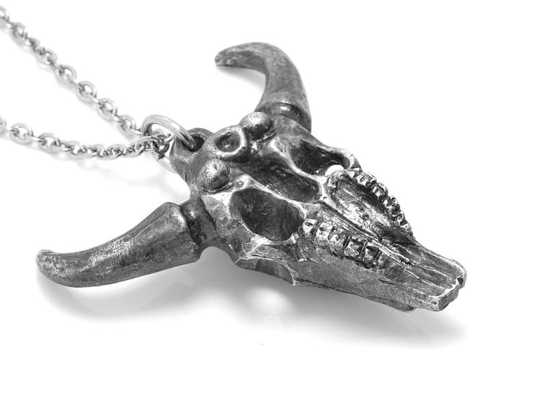 May include: A silver bull skull pendant necklace. The skull is detailed with teeth and horns. The chain is silver and has a lobster clasp.