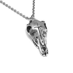 May include: A silver necklace with a detailed skull pendant. The pendant is a realistic depiction of an animal skull, with a textured surface and visible teeth.