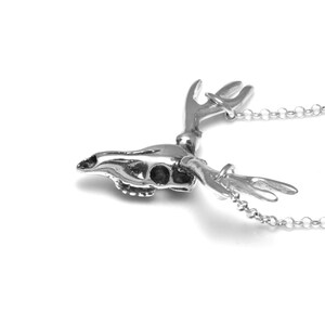 May include: A silver deer skull pendant necklace with detailed antlers. The pendant is attached to a silver chain.