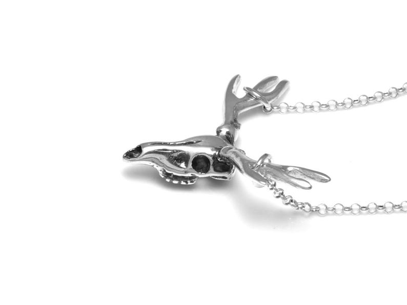 May include: A silver deer skull pendant necklace with detailed antlers. The pendant is attached to a silver chain.