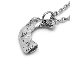 May include: A silver necklace with a pendant shaped like a bone. The pendant is textured and has a rough, organic look.